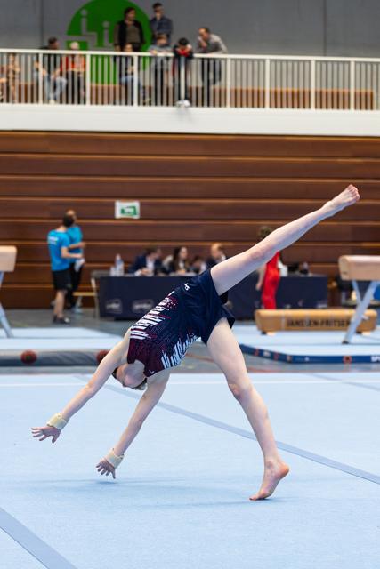 Gymnast performs cartwheel on floor mat with extended limbs during routine in indoor sports hall with spectators
