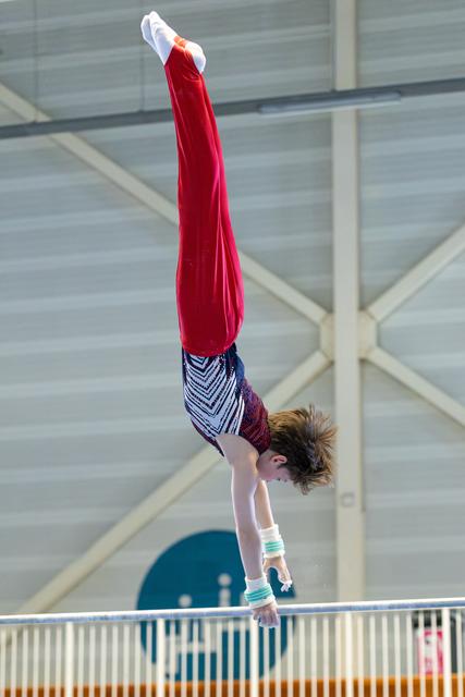 Athlete performs vertical handstand in mid-air above apparatus, body fully extended with pointed toes during routine