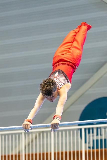 Young athlete performs a handstand on horizontal bar, demonstrating strength and control during routine