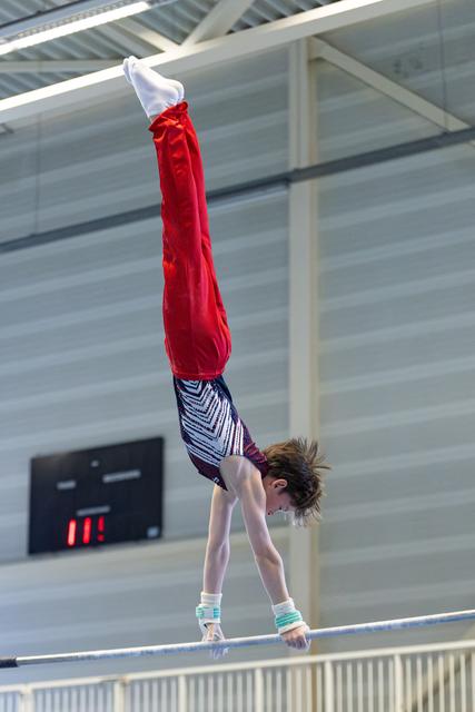 Young athlete performing handstand on parallel bars in indoor sports hall, demonstrating strength and balance
