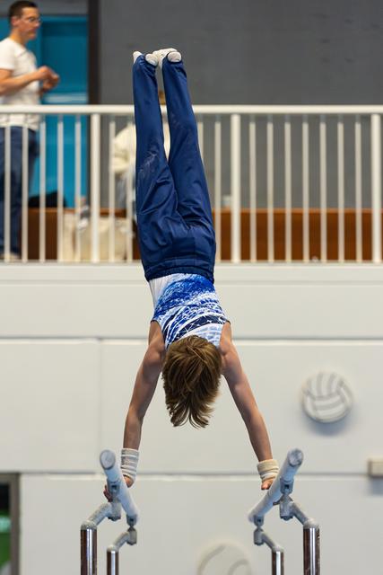 Young athlete performing a handstand on parallel bars during a routine, displaying strength and balance in competition
