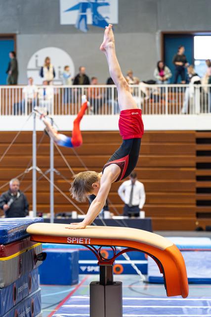 Young athlete performing a handstand on the vault table during routine, body fully extended with legs split upward