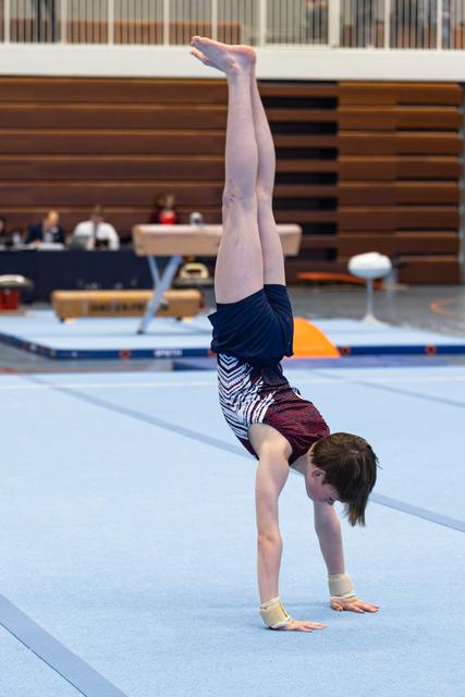 Athlete performs a handstand on floor exercise mat, displaying strength and balance with straight legs extended upward
