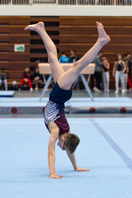 Young athlete performs a handstand with extended legs during floor routine at indoor gymnastics event