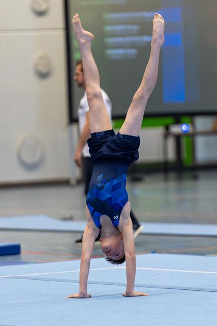 Young athlete performs a vertical handstand with legs split apart on training mat in indoor sports facility