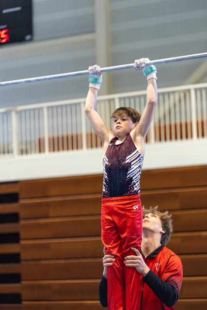 Young athlete grips the high bar while coach spots from below, arms ready to support during training routine