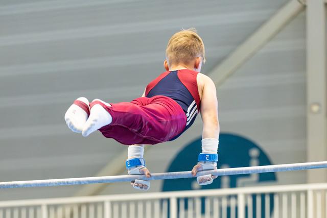 Young athlete performs aerial release move on horizontal bar, demonstrating precise form and body control during routine