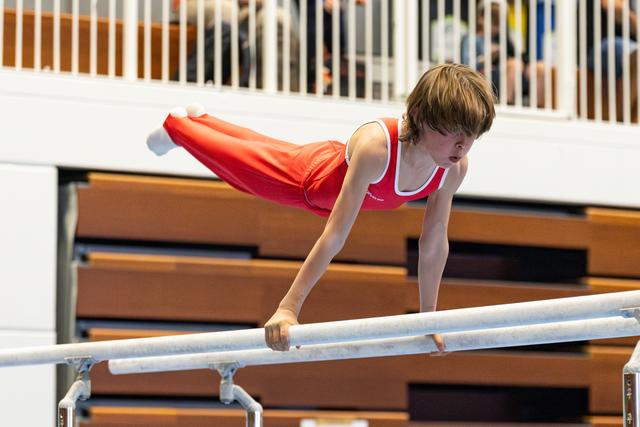 Young athlete performing horizontal hold on parallel bars during routine, body extended parallel to equipment in gymnasium