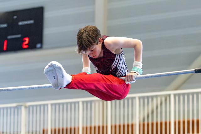 Young athlete performing horizontal bar routine with extended body position, displaying focus and strength during competition