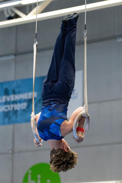 Athlete performs an inverted hang on still rings, displaying strength and control with legs extended upward in an indoor gym