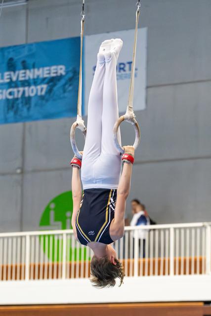Young athlete performs inverted hang on rings during routine at indoor sports venue
