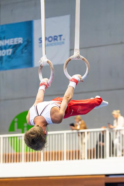 Athlete performing an inverted hang on still rings, body fully extended with pointed toes during routine