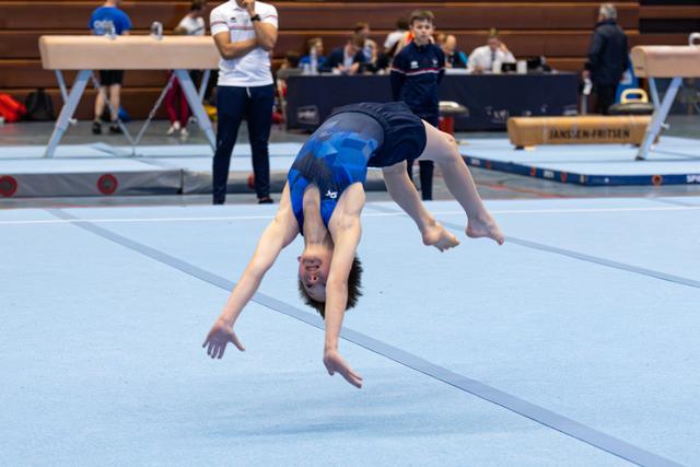 Athlete performing a back flip mid-air during floor exercise routine at an indoor gymnastics meet