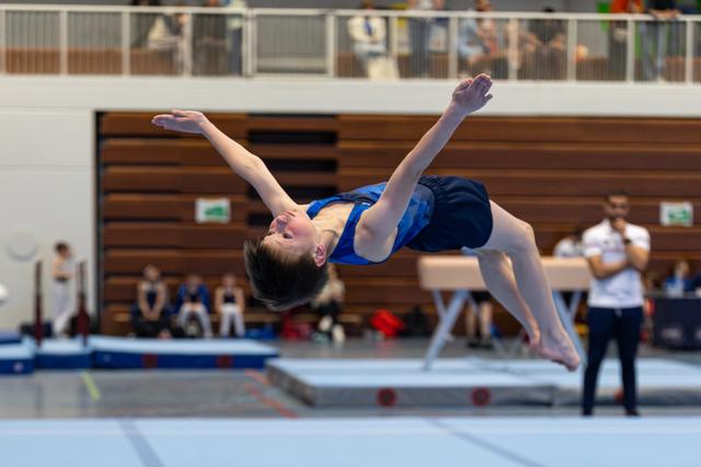 Young athlete performs an inverted aerial move during floor exercise, body fully extended in mid-air at indoor sports hall