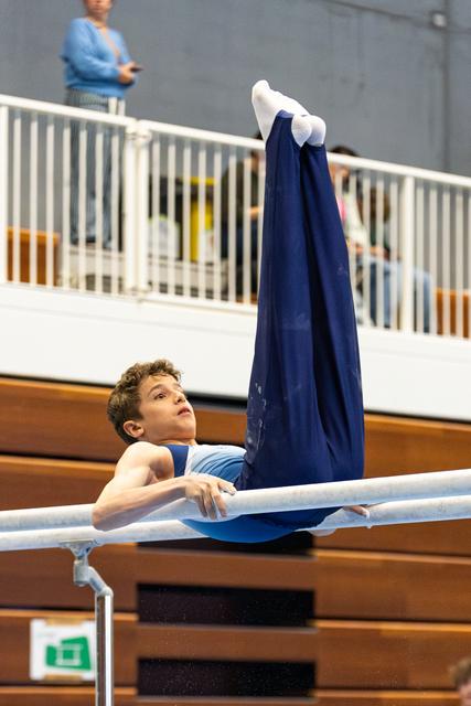 Athlete performs parallel bars routine with legs extended upward, displaying strength and control in gymnasium