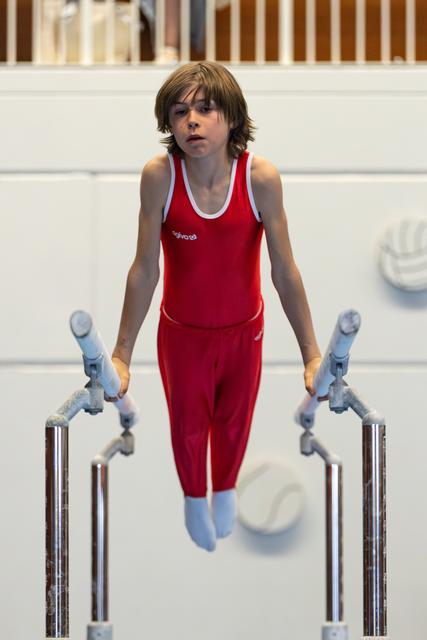 Young gymnast in red uniform performing on parallel bars, displaying intense focus and concentration during routine