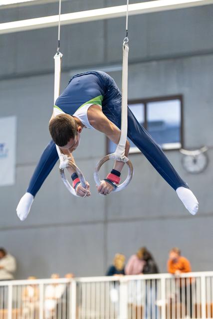 Athlete performing inverted pike position on still rings during competition, demonstrating strength and control in modern facility