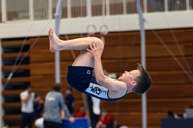 Athlete performs a tight tuck flip on trampoline during indoor event, demonstrating control and form in mid-air