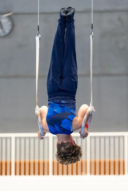 Young athlete performing an inverted hang on still rings, body fully extended upside down during training