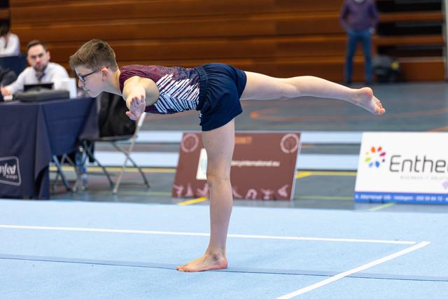Young athlete holds an arabesque balance during floor exercise, arms extended with focused concentration