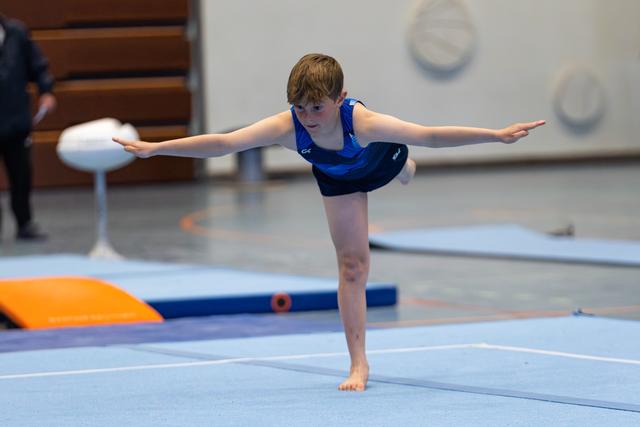 Young athlete performs an arabesque balance on training mat, arms extended horizontally, demonstrating control and poise