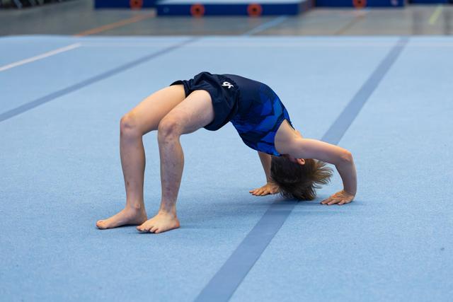 Young athlete performing backbend on blue training floor, demonstrating flexibility and strength during practice session