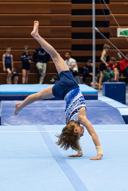 Young athlete performs backbend on floor mat during training session, demonstrating flexibility with one leg extended upward