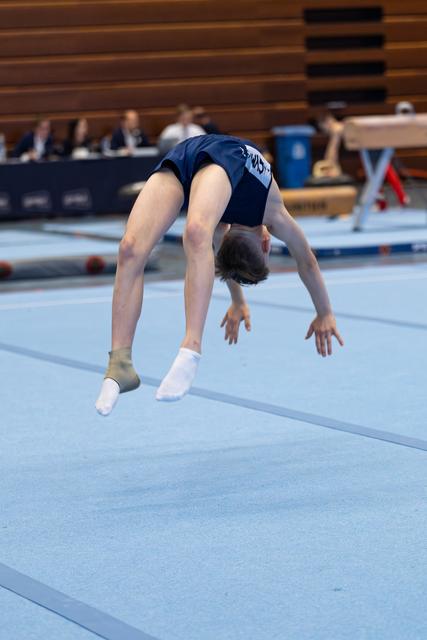 Young athlete performs a backbend during floor exercise routine at indoor gymnastics meet with judges in background