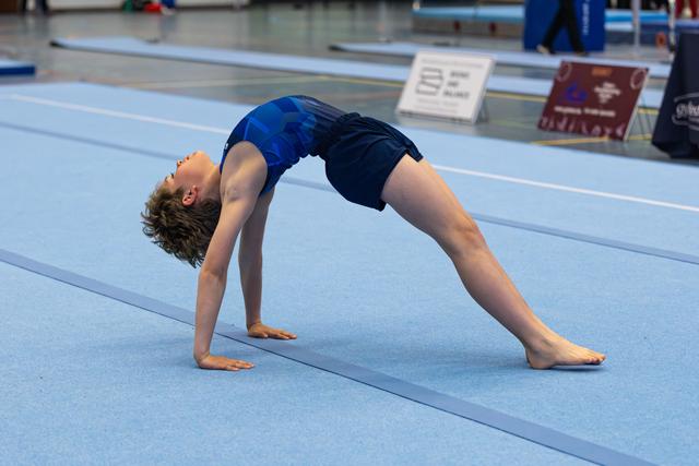 Young athlete performing a backbend stretch on blue mat during training, displaying flexibility and form