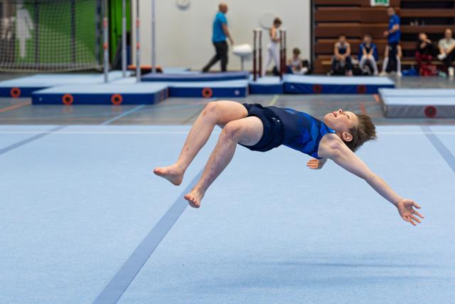 Young athlete performing a backflip mid-air on floor exercise mat during training session at indoor sports facility