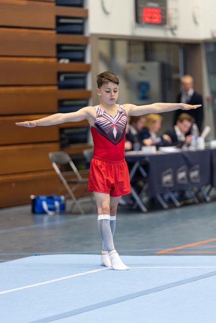 Young athlete performing a balance pose with outstretched arms during a floor routine at an indoor competition