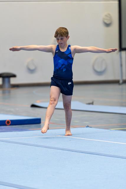 Young athlete performs a balance position with arms extended on a light blue floor mat during training