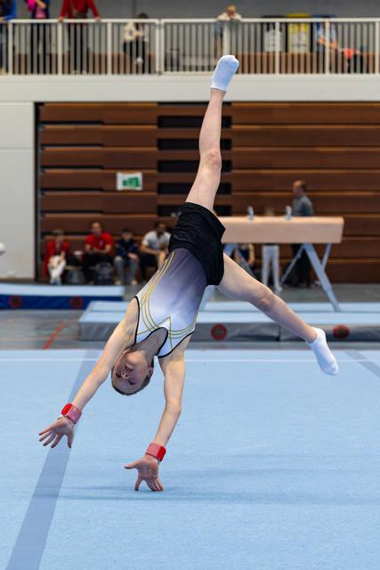 Young gymnast performs a cartwheel on floor exercise mat, wearing white and black leotard with red wrist guards