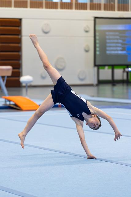 Young gymnast performs a one-armed cartwheel on the floor mat, demonstrating flexibility and balance in a training facility
