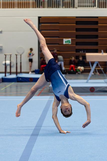 Young athlete performing a one-handed cartwheel on blue floor mat during training session in indoor gymnasium