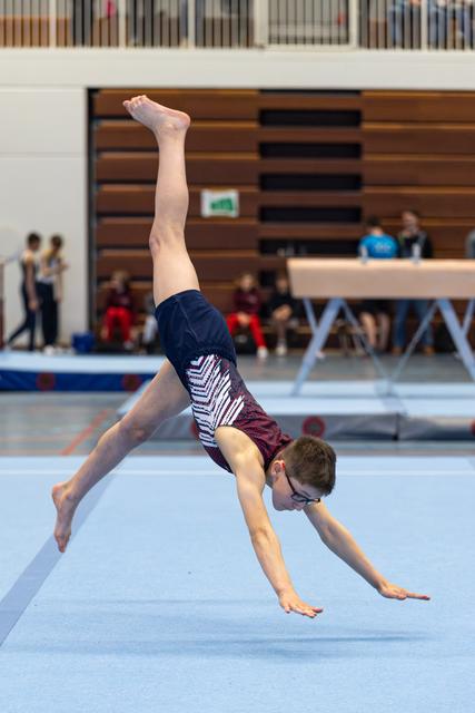 Young athlete performs a cartwheel on floor exercise at an indoor competition, showing impressive form and flexibility