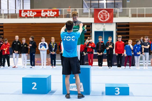 First place winner applauds from podium while other athletes stand at attention during medal ceremony in sports hall