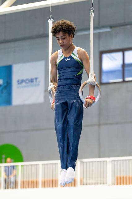 Athlete in navy uniform concentrates while suspended on rings, displaying focus and control in indoor training facility