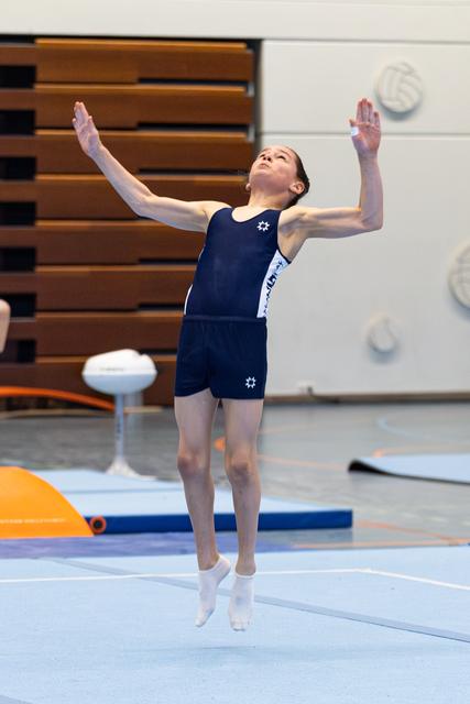 Young gymnast performs floor exercise with arms raised upward, displaying graceful form in indoor training facility