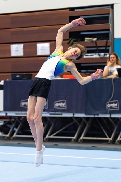 Young gymnast performs expressive floor routine with dramatic side bend, arms extended, at indoor competition venue