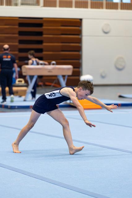 Young athlete performs a deep lunge position during floor exercise routine on blue training mat in gymnasium