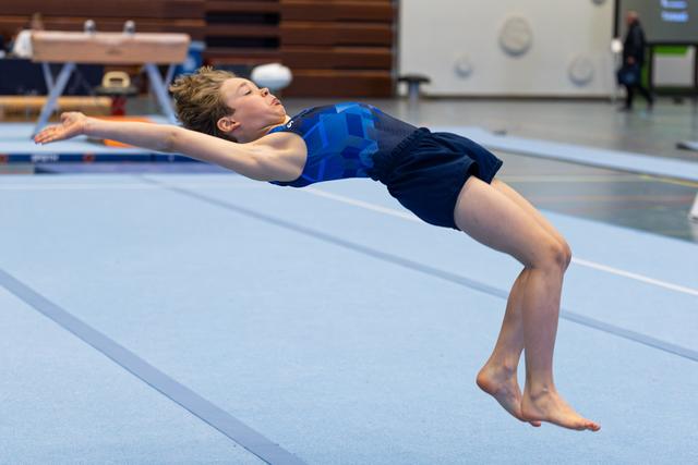 Young athlete performs floor routine with arched back extension, arms stretched overhead in gymnastics training facility