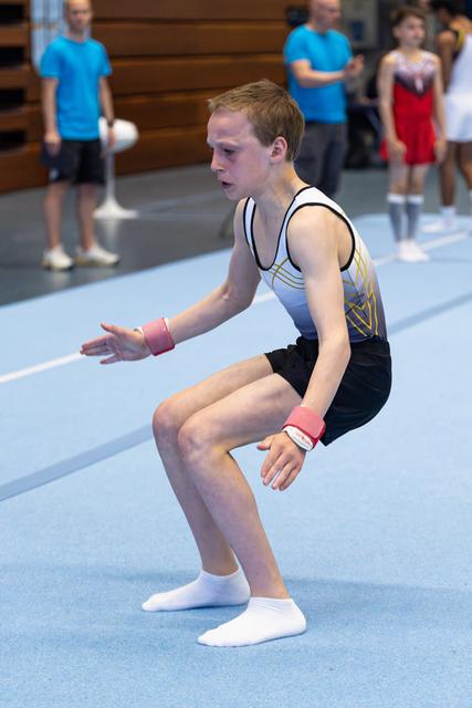 Young athlete performing floor routine with intense concentration, arms positioned mid-movement on blue spring floor