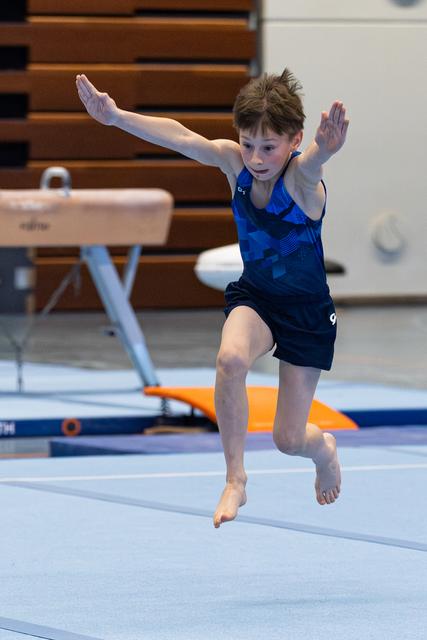Young athlete performs floor routine with arms raised mid-leap in indoor training facility