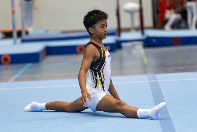 Young gymnast performing a split on floor mat, displaying concentration and flexibility during training session