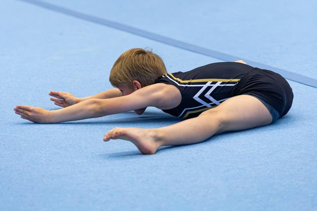 Young gymnast performing a forward fold stretch in splits position on blue floor mat during training