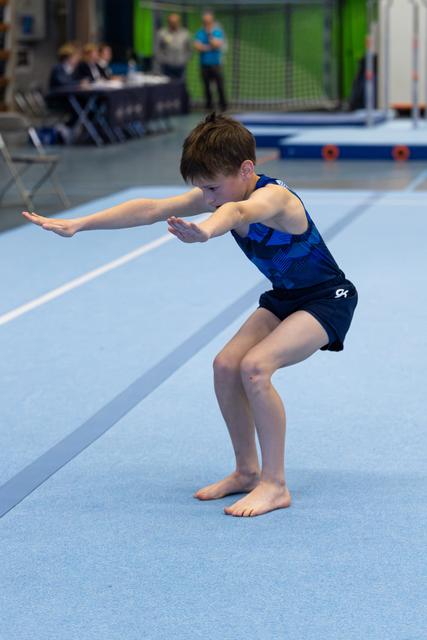 Young athlete in blue leotard concentrates in deep squat position during floor exercise routine at indoor training facility