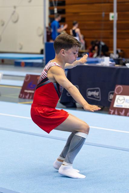 Young athlete in red outfit and knee-high socks maintains a focused squat position during floor exercise routine