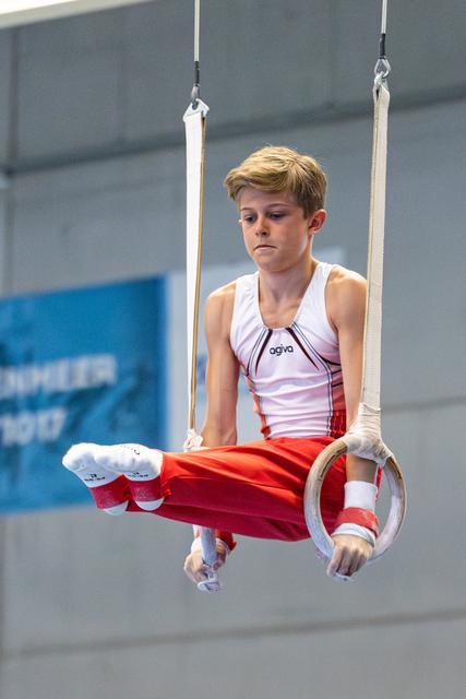 Young athlete performs on rings with intense concentration, body horizontal, wearing white and red uniform