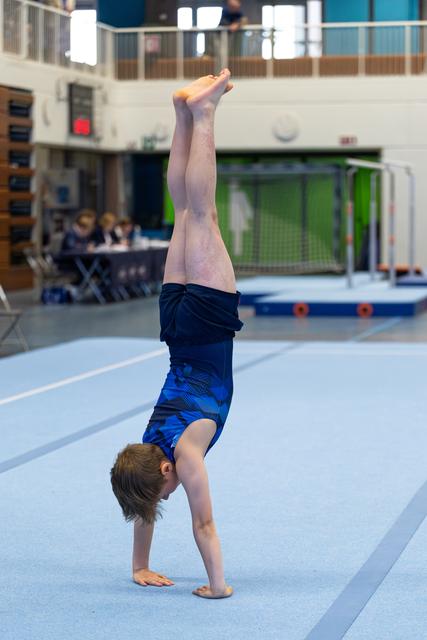 Young gymnast performing a handstand on blue spring floor during training, demonstrating balance and body control